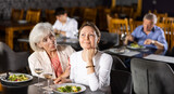 Young girl having lunch at restaurant talking with elderly friend mom. Sad upset young woman shares with mature female friend talks about difficulties of interpersonal communication in team at work.