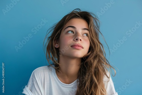 Pensive portrait of a young woman looking up, free space for text, pale blue background, studio photo 