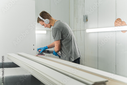 young man with headphones sanding wood with orbital sander in a workshop. High quality photo
