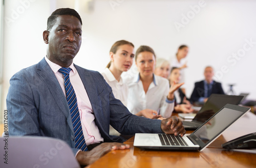 African-american businessman using laptop during conference in meeting room. Man sitting at desk with colleaugues.