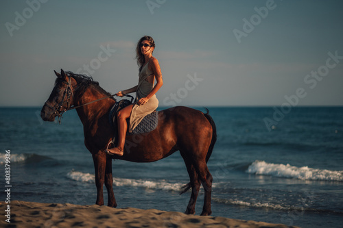 Side view of an attractive woman riding a horse on a beach during a dusk