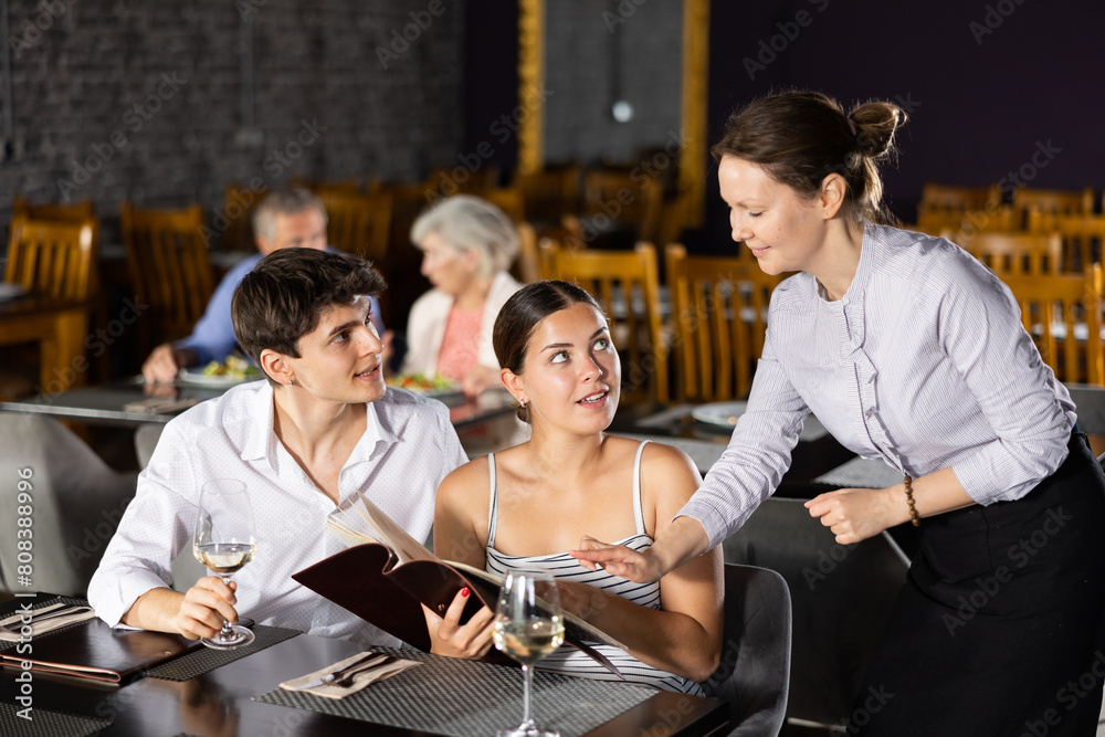 Obraz premium Adult woman waiter takes order from couple of young men and women in restaurant