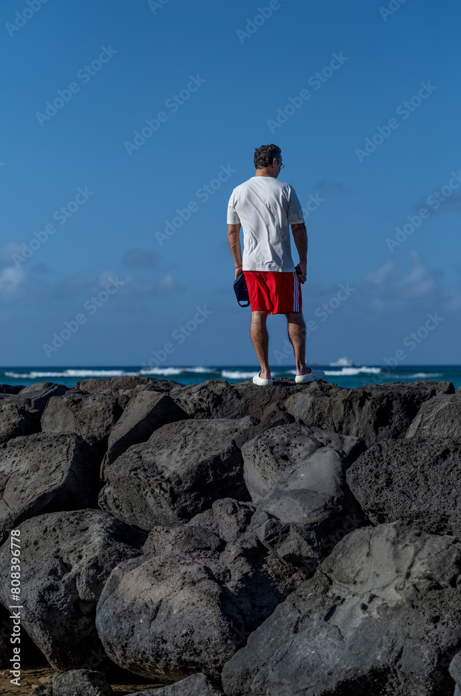 Surfer Standing on Rocks Checking Out the Waves .