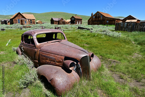 Beneath the clear blue summer sky, a rusting car sits in Bodie, California.
 photo
