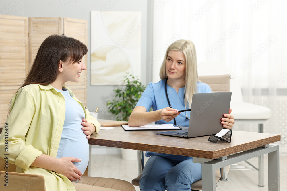 Doctor consulting pregnant patient at table in clinic Doctor consulting pregnant patient at table in clinic