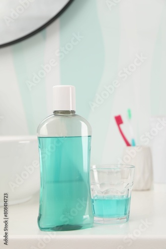 Bottle of mouthwash, toothbrushes and glass on white table in bathroom