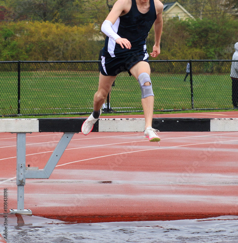 Runner puching off the steeplchase barrier over the water pit