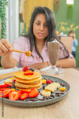 Woman eating pancakes with honey and milkshake in a chocolate restaurant