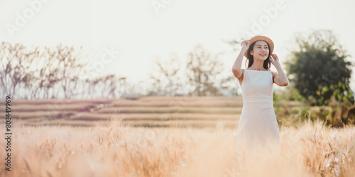 Woman in a white dress and straw hat standing amidst a golden wheat field at sunset.