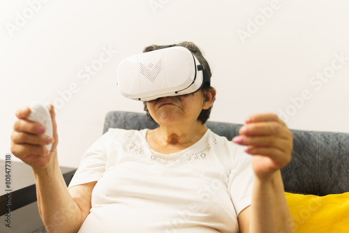 A senior woman wearing a white shirt is playing a video game with a remote in her hand