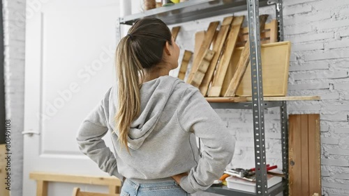 Rear view of a young hispanic woman in a workshop surrounded by lumber and tools, denoting creativity and craftsmanship.