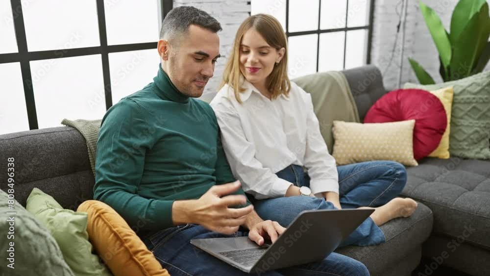 A man and woman interact joyfully while using a laptop in a cozy living room with colorful pillows. A man and woman interact joyfully while using a laptop in a cozy living room with colorful pillows.