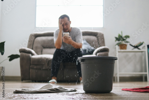 Stressed Man Calling Home Service to Repair Roof Leak at Home. Putting a  Bucket for Water From The  Leaks Roof.