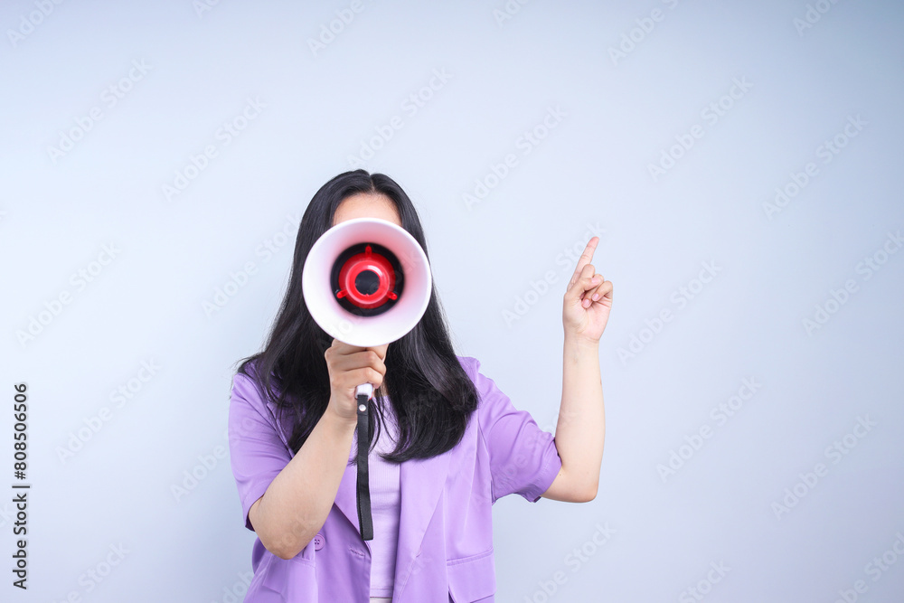 Fototapeta premium Woman shouting and holding megaphone while pointing to the side on grey background