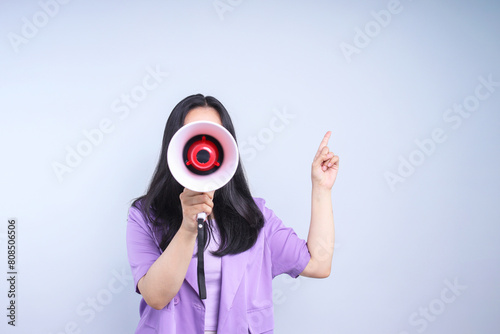 Woman shouting and holding megaphone while pointing to the side on grey background