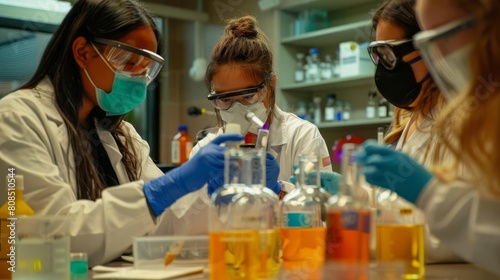 Chemistry students conduct an experiment in a lab. They wear goggles and gloves to protect themselves from chemicals.