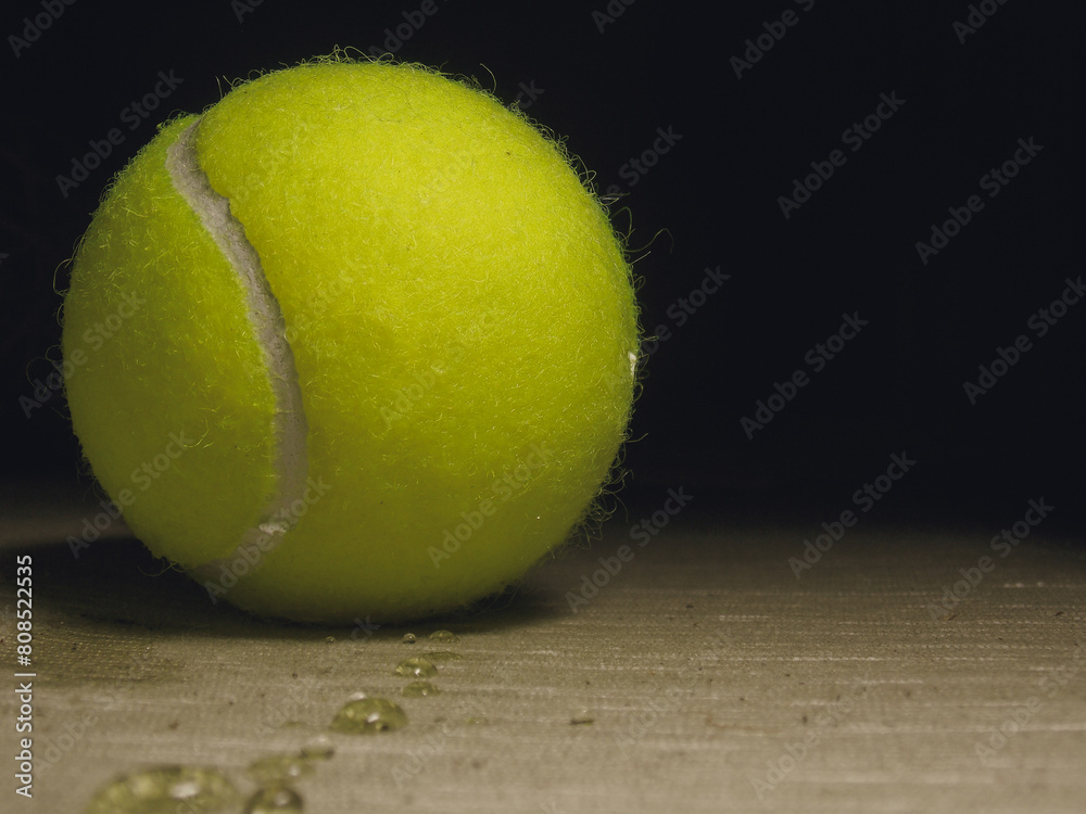 Close up of wet yellow tennis ball with black copy space and water droplets