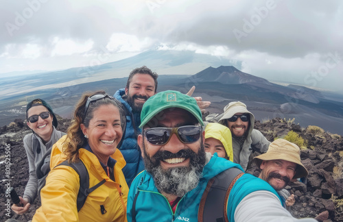 A selfie of a group of happy people on top of a mountain, with mountains and a volcano in the background