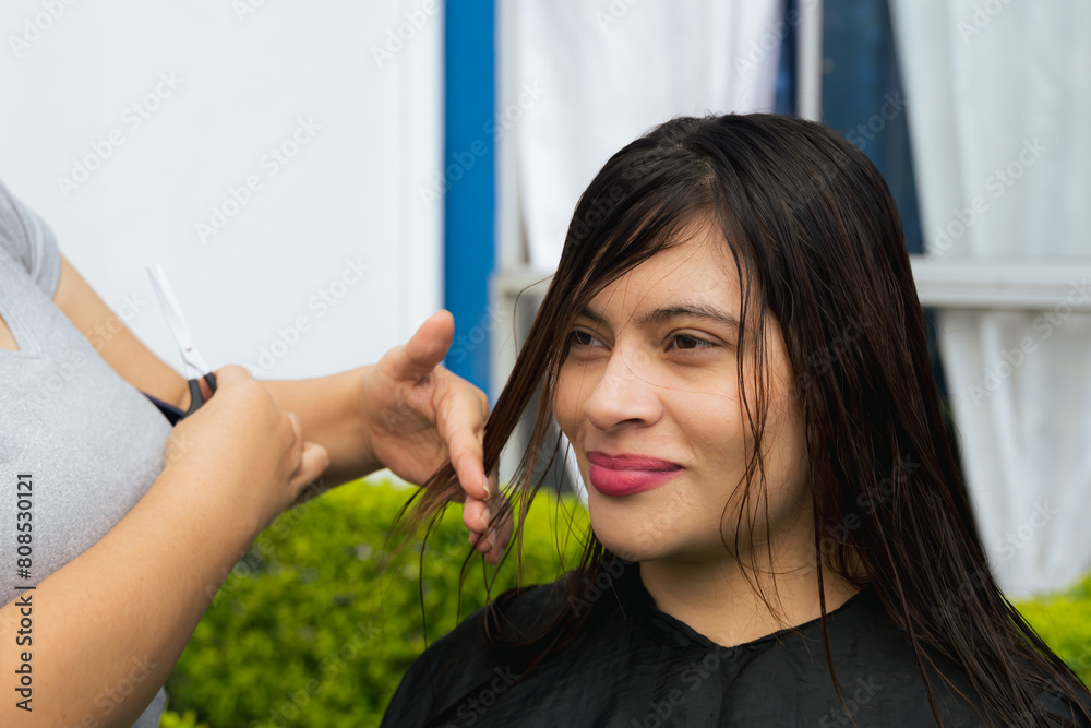 Obraz premium Latina mother stylist cutting her daughter's dark hair outdoors. Concept of love and beauty. Mother and daughter.