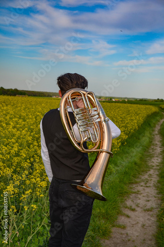 A young man in a white shirt stands on a dirt road with a trumpet - tenor saxhorn