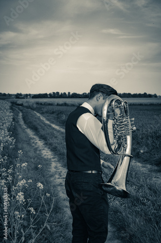 A young man in a white shirt stands on a dirt road with a trumpet - tenor saxhorn photo