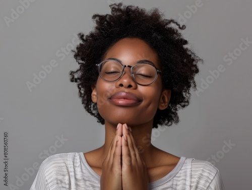 A woman with curly hair is wearing glasses and praying. She has a peaceful and serene expression on her face