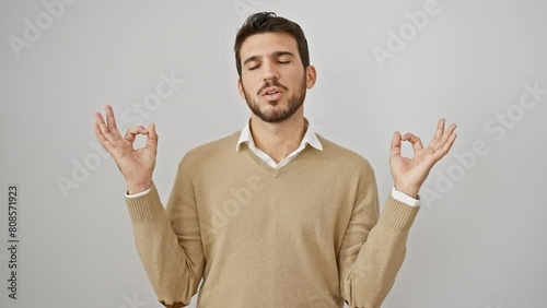 Beaming young hispanic guy meditating, calm eye-closed pose. radiant health and peaceful life expressed through yoga, wearing sweater and standing, relaxed on isolated white background. photo