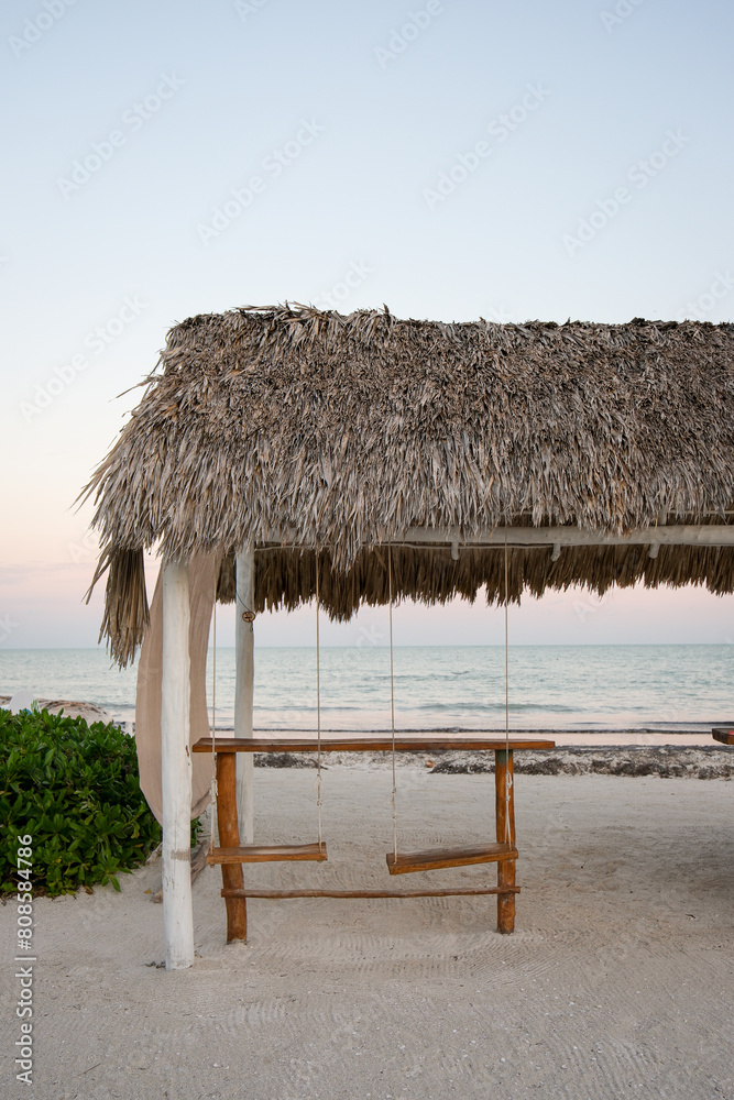 Two empty swings underneath a thatched roof on the beach in Mexi Two empty swings underneath a thatched roof on the beach in Mexi