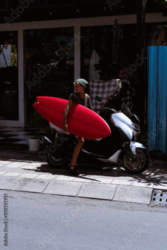 Portrait young happy stylish woman with a surfboard on a motorbike.