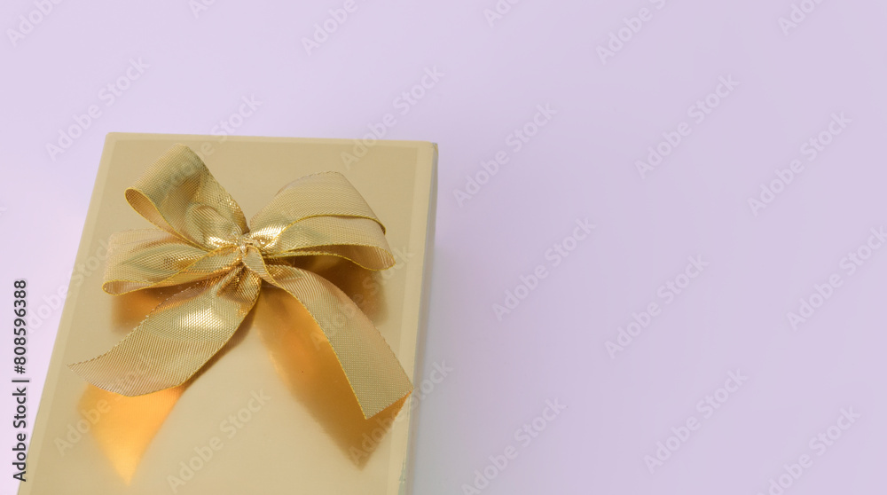 A gold bow is tied around a gift box on a soft pink background. Banner. Copy space A gold bow is tied around a gift box on a soft pink background. Banner. Copy space