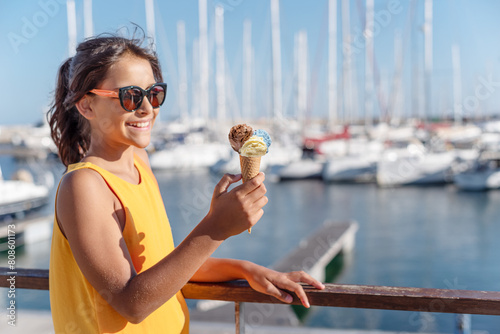 Happy, smiling girl holding ice cream cone with colorful ice cream balls. Sunny sea coastline at the background.