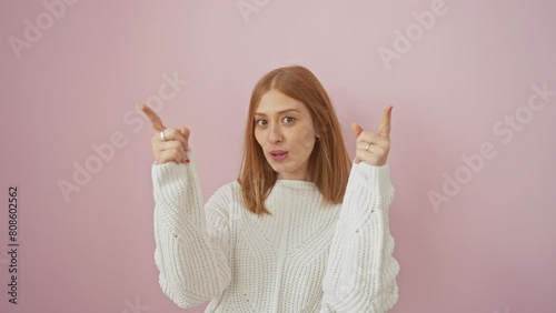 Amazed young redhead woman in a cozy sweater looks up, pointing in surprise at an invisible lottery on a vibrant pink background. her eyes wide with joy, her confidence beams unabated. photo