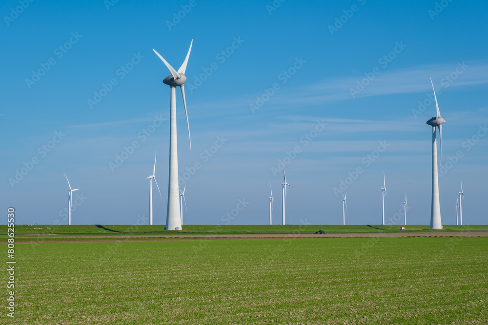 A large field of green grass stretches out, with numerous windmills towering in the background, their blades spinning in the wind A large field of green grass stretches out, with numerous windmills towering in the background, their blades spinning in the wind