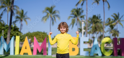 Kid near Miami Beach sign. Kid enjoy summer vacation holiday. Travel, childhood happiness concept. Summer Holiday at Miami Beach Florida. Blond little kid boy having fun on Miami beach, Ocean drive.