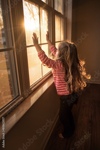 Little girl with long blonde curls looking out sunny window photo