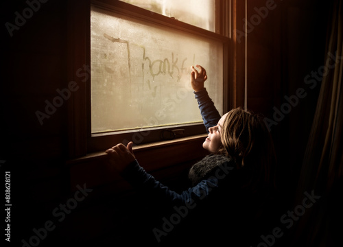 Happy child writing thankful on window sill