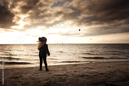 Young girl watching kite boarders at sunset photo