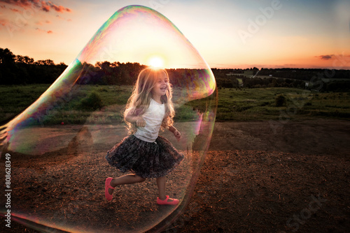 Happy little girl playing in giant colorful bubble outdoors