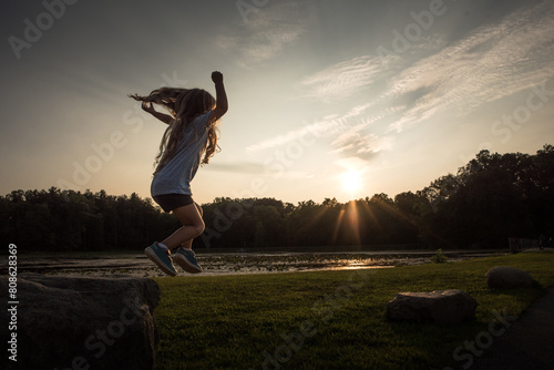 Little girl with long curls jumping off rock with arms in air photo