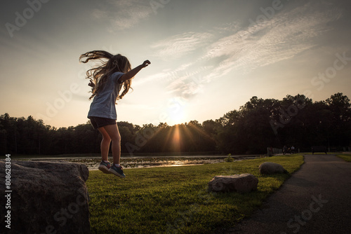 Little girl with long curls jumping off rock near lake in summer photo