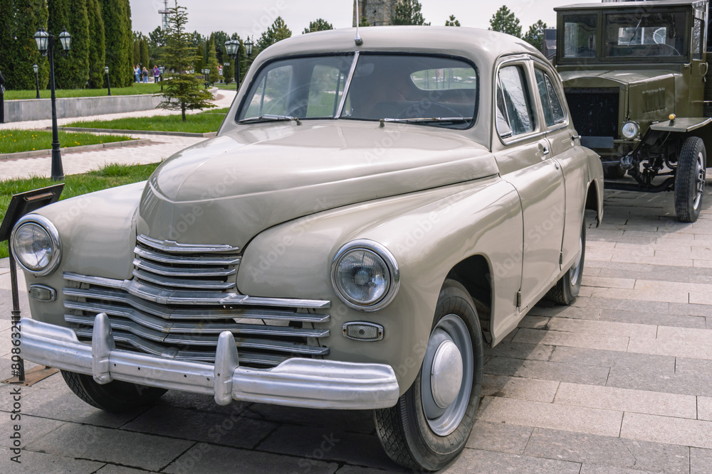 An old middle-class passenger car. The body of the old car is made of beige all-metal material. Metal bumper and chrome grille of an old retro car.