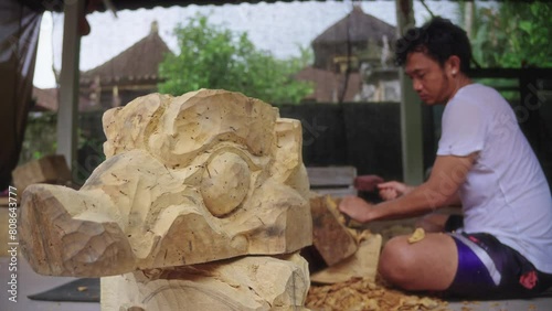 Barong Bangkal Mask With A Balinese Wood Carver Working In The Background. - closep shot photo