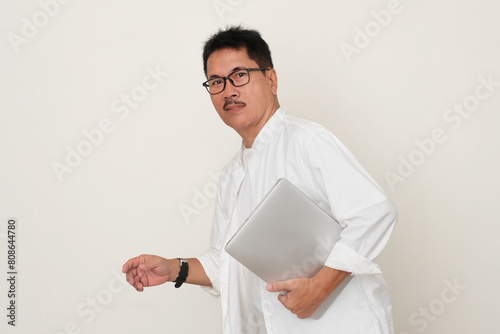 Man at home in casual clothes, walking with his left hand carrying a laptop photo