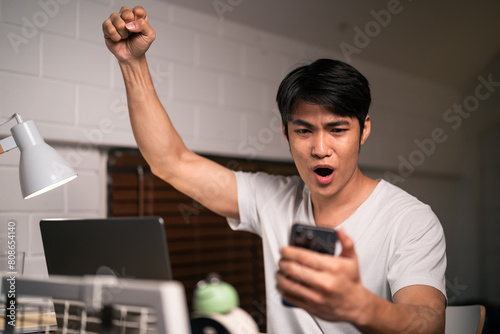 Asian young man overworking and using mobile phone check news at night. 