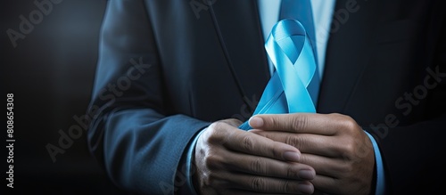 A middle aged person holds a blue ribbon in their hand symbolizing support care and charity for prostate cancer awareness The closeup image portrays the concept of medicine and oncology urging help f photo