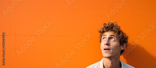 A young attractive man stands before an orange wall his face displaying a mix of shock and astonishment His jaw hangs open in disbelief as he contemplates something truly incredible The scene is perf