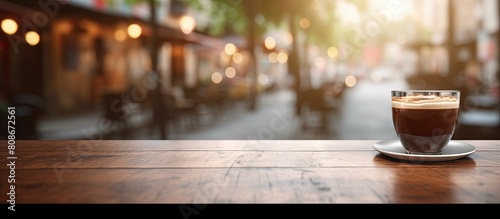 The image features a wood table with no objects on it set against a blurry background of a coffee shop with bokeh effects. Copy space image. Place for adding text and design