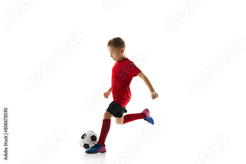 Little athlete boy, training dribbling ball and passing in motion against white studio background. Young soccer player. Concept of professional sport, championship, youth league, hobby. Ad © Lustre