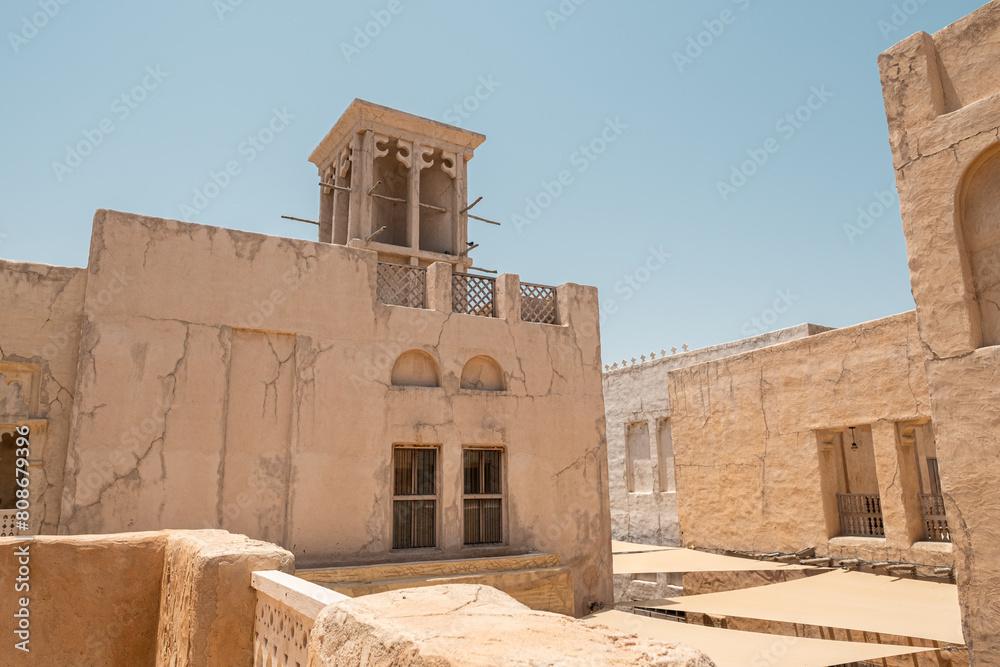 House in traditional Arabic architecture with wind tower. Traditional Arabic style building with windcatcher tower and palm leaves thatched roof. Old Dubai, UAE. View of rooftops of old Arab city