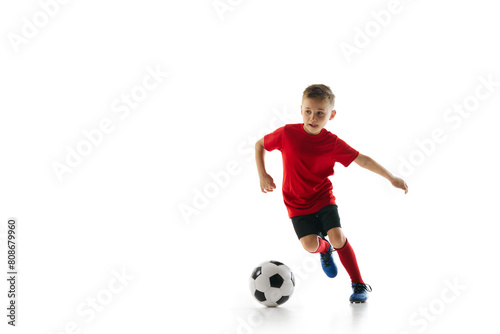 Athletic, sportive boy in uniform training dribbling technique in motion against white studio background. Dynamic shot. Concept of professional sport, championship, youth league, hobby. Ad